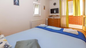 A bedroom with a bed, a TV, a window with curtains, a radiator, and a small cabinet. - 1 bedroom beautiful apartment in Brela (Brela)