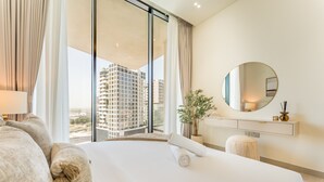 Een hotelkamer met een groot bed, een ronde spiegel, een plant in pot en uitzicht op wolkenkrabbers.