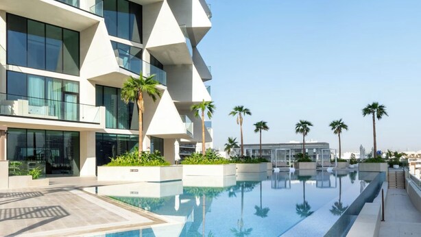 Een modern hotel met een zwembad, palmbomen en een heldere lucht.
