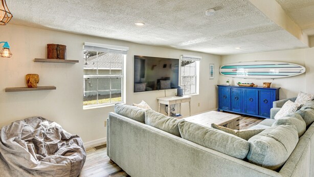 A living room with a grey sofa, a bean bag, a blue cabinet, and a surfboard on the wall. - < 1 Mi to Ramp! Boater's Retreat in Edgewater (Edgewater)