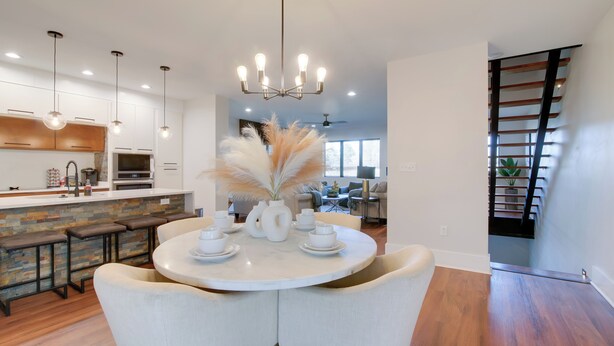 A modern kitchen with white cabinets, a central island with stools, and a dining area with a round table and chairs. - Walk to FedEx Forum! Luxe Townhome w/ Rooftop Deck (Memphis)