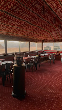 A dining area with tables and chairs, a patterned ceiling, and a view of a desert landscape through large windows.. Desert Magic Camp &