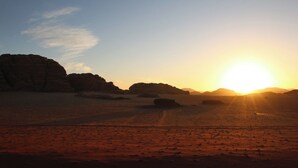 A desert landscape with a sunset, featuring large rock formations and a clear sky.