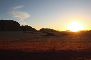 A desert landscape with a sunset, featuring large rock formations and a clear sky. - Desert Magic Camp &  (Wadi Rum)
