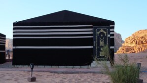 A tent-like structure with a black and white striped exterior, a decorative door, and a desert landscape with rocks and sparse vegetation.