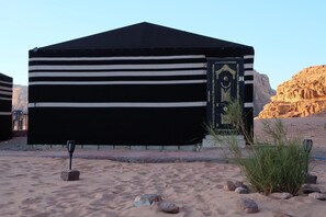 A tent-like structure with a black and white striped exterior, a decorative door, and a desert landscape with rocks and sparse vegetation. - Desert Magic Camp &  (Wadi Rum)