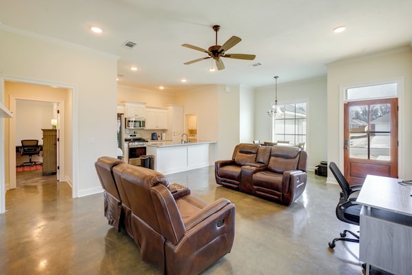 A spacious living room with leather recliners, a dining area with a table and chairs, a kitchen in the background, and a ceiling fan.