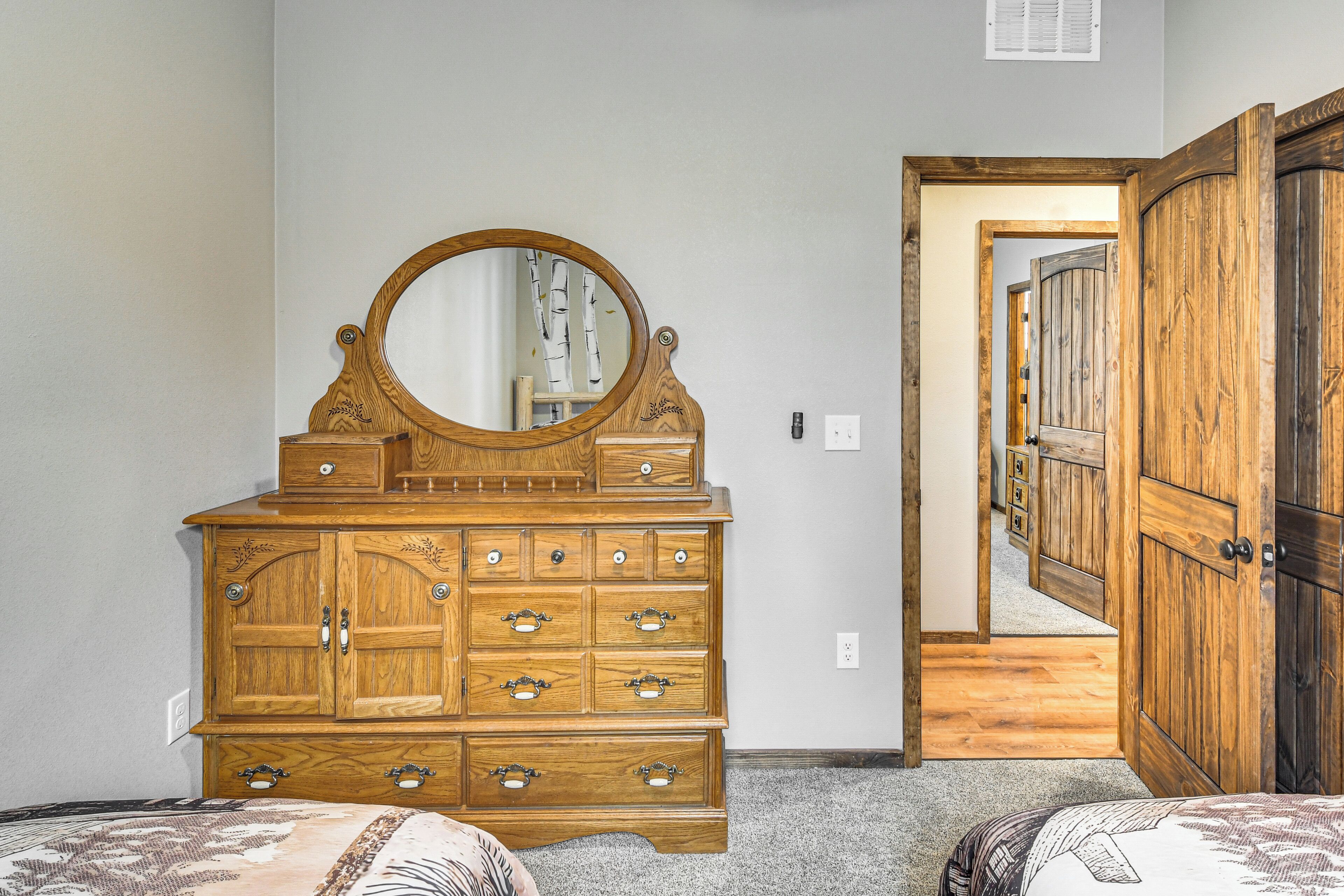 Une chambre avec une commode en bois, un grand miroir et une porte donnant sur une autre pièce.