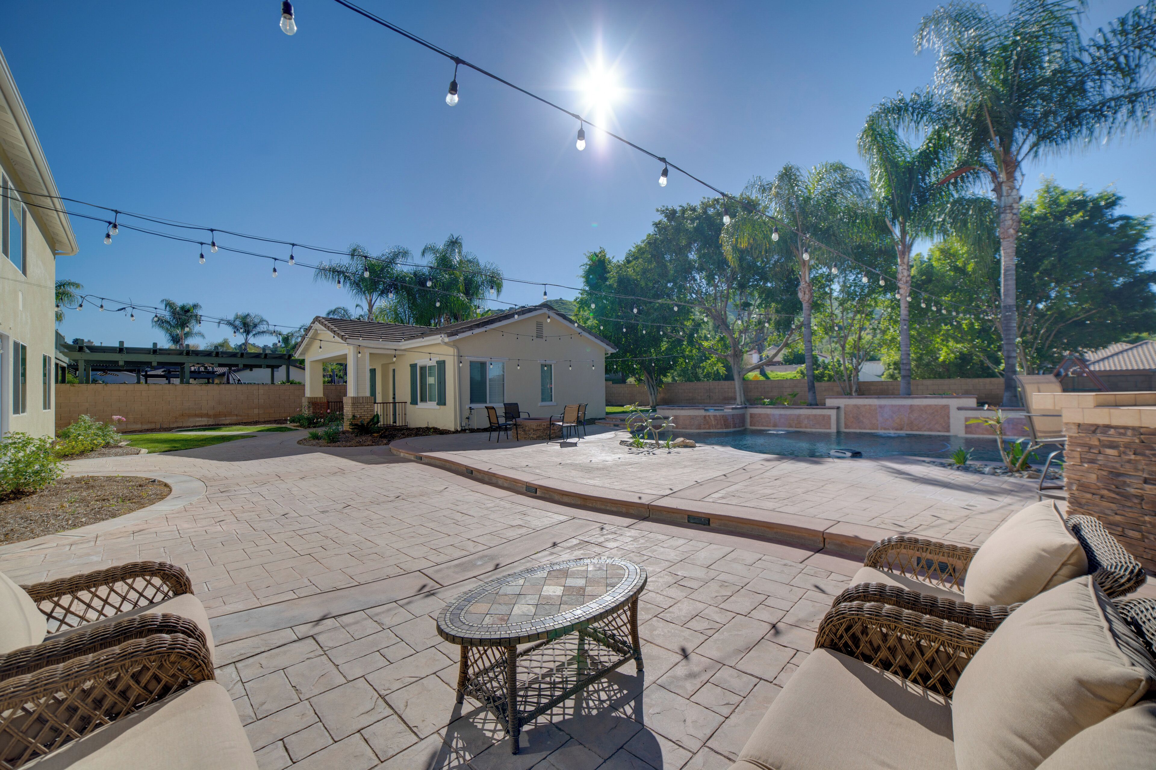 A backyard with a patio, outdoor furniture, a swimming pool, and a house.