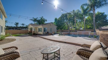 A backyard with a patio, outdoor furniture, a swimming pool, and a house.