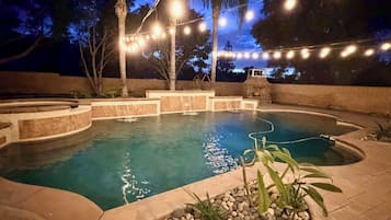 A swimming pool with a curved design, surrounded by a stone deck and palm trees.