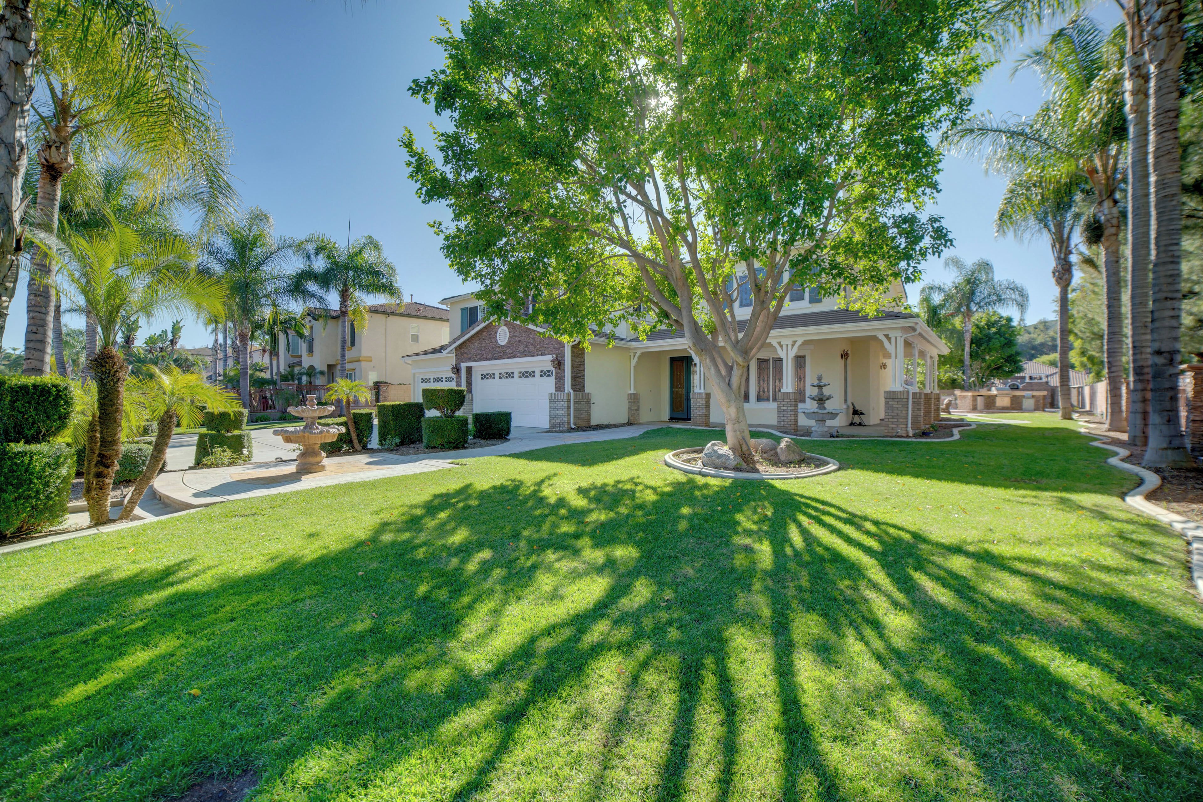 A residential property with a well-maintained lawn, a large tree, and a brick house with a garage.