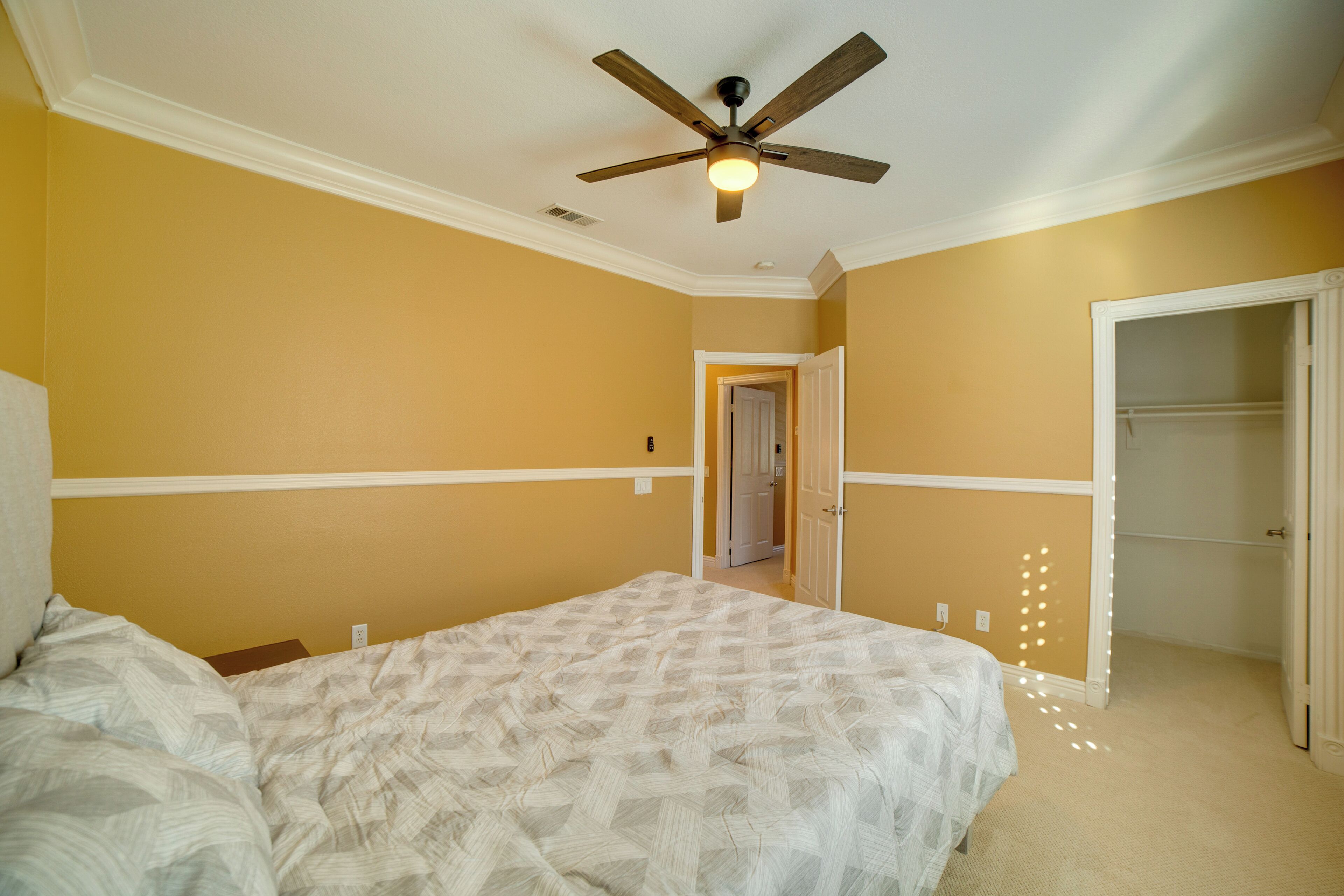 A bedroom with a bed, a ceiling fan, and a door leading to another room.
