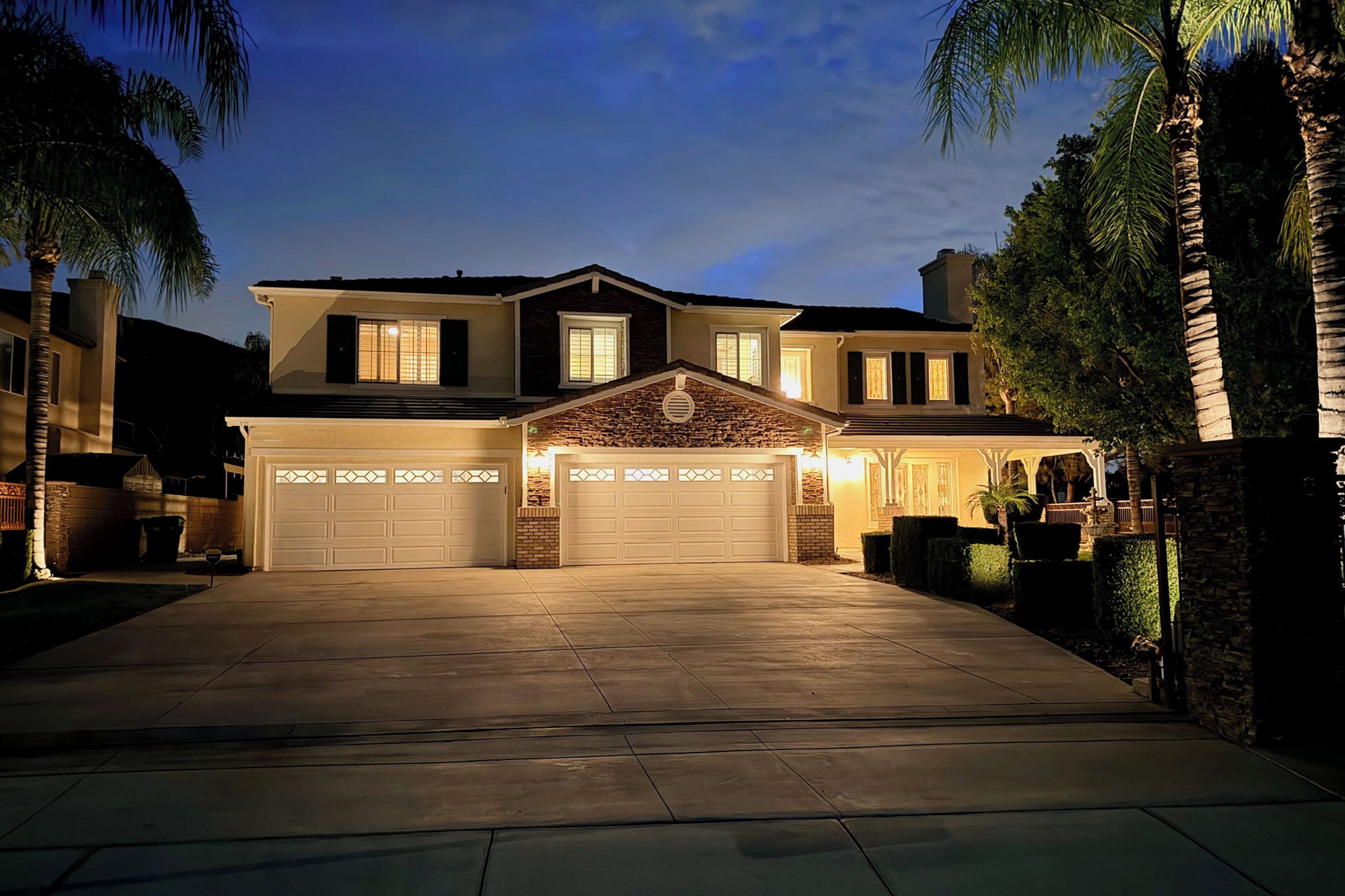 A two-story house with a garage, a stone facade, and a well-lit driveway.