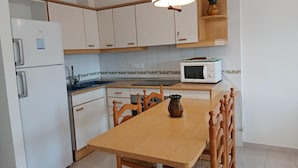 Een keuken met witte kasten, een houten eettafel, een witte koelkast, een magnetron en een hangende lamp.