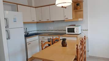 A kitchen with white cabinets, a wooden dining table, a white refrigerator, a microwave, and a hanging light fixture.