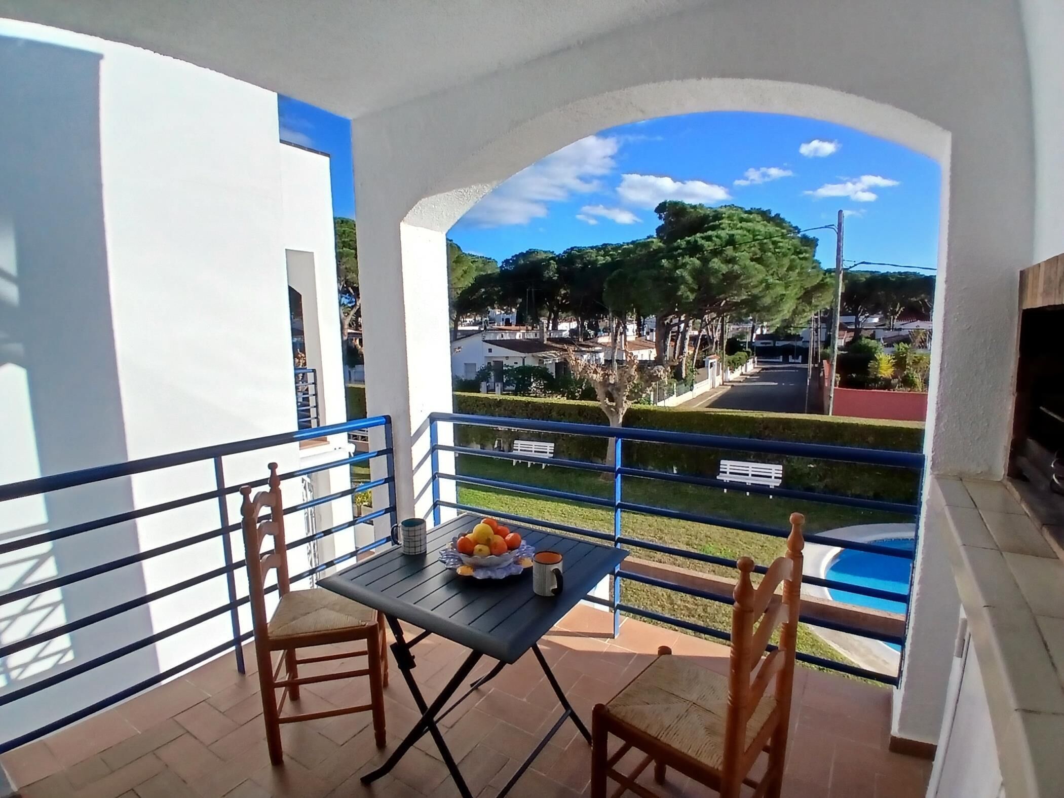 Ein Balkon mit Tisch und Stühlen, einer Obstschale und Blick auf eine Wohngegend mit Bäumen und Häusern.
