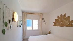 Een slaapkamer met een bed, een raam met gordijnen, een decoratie aan de muur en een wandlamp.