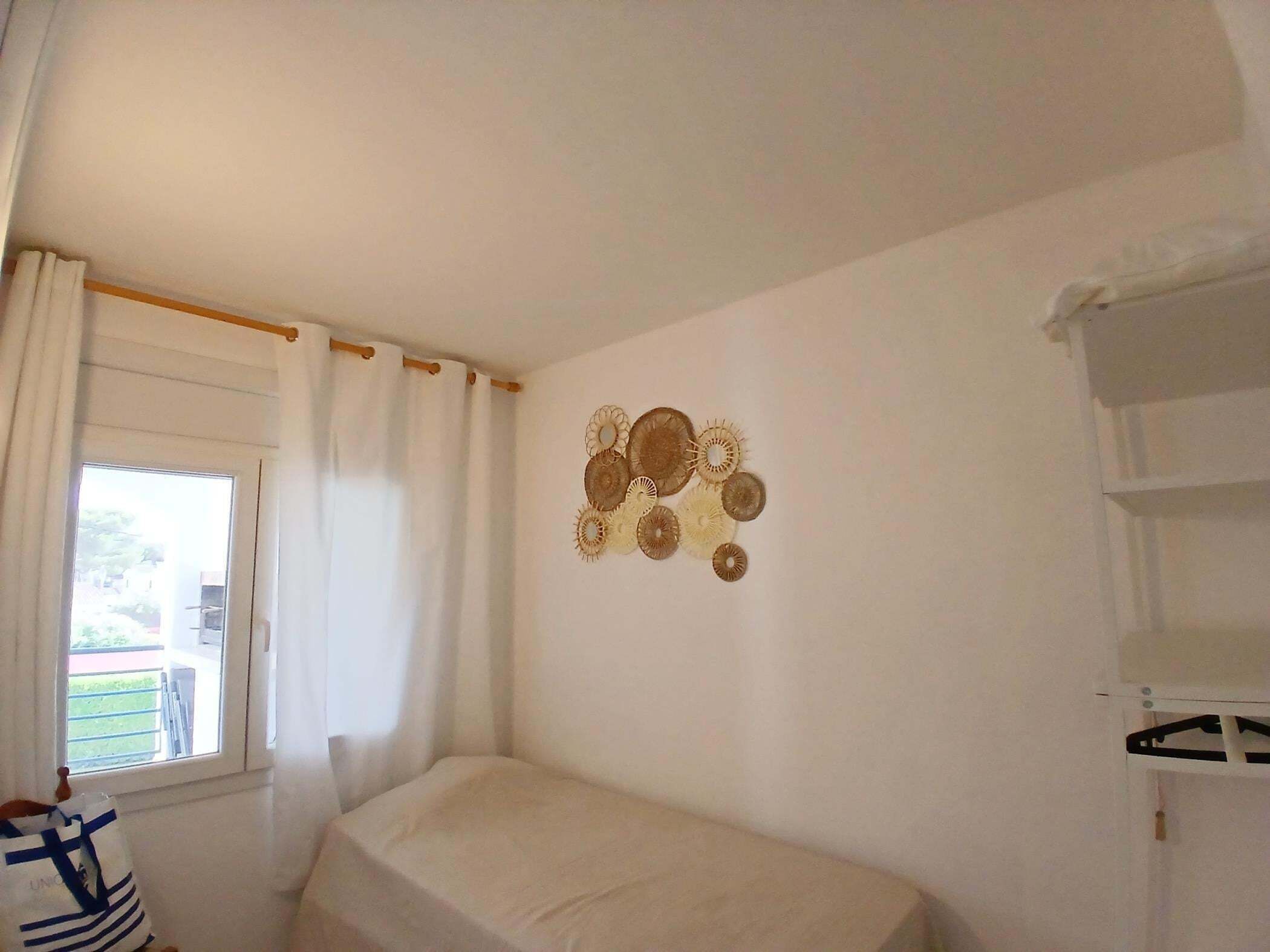Un dormitorio con cama, ventana con cortinas, decoración en la pared y una estantería blanca.