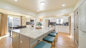 A spacious kitchen with a central island, bar stools, and a dining area with a table and chairs. - Groups Welcome, Central Location! Tulsa Gem + Yard (Tulsa)