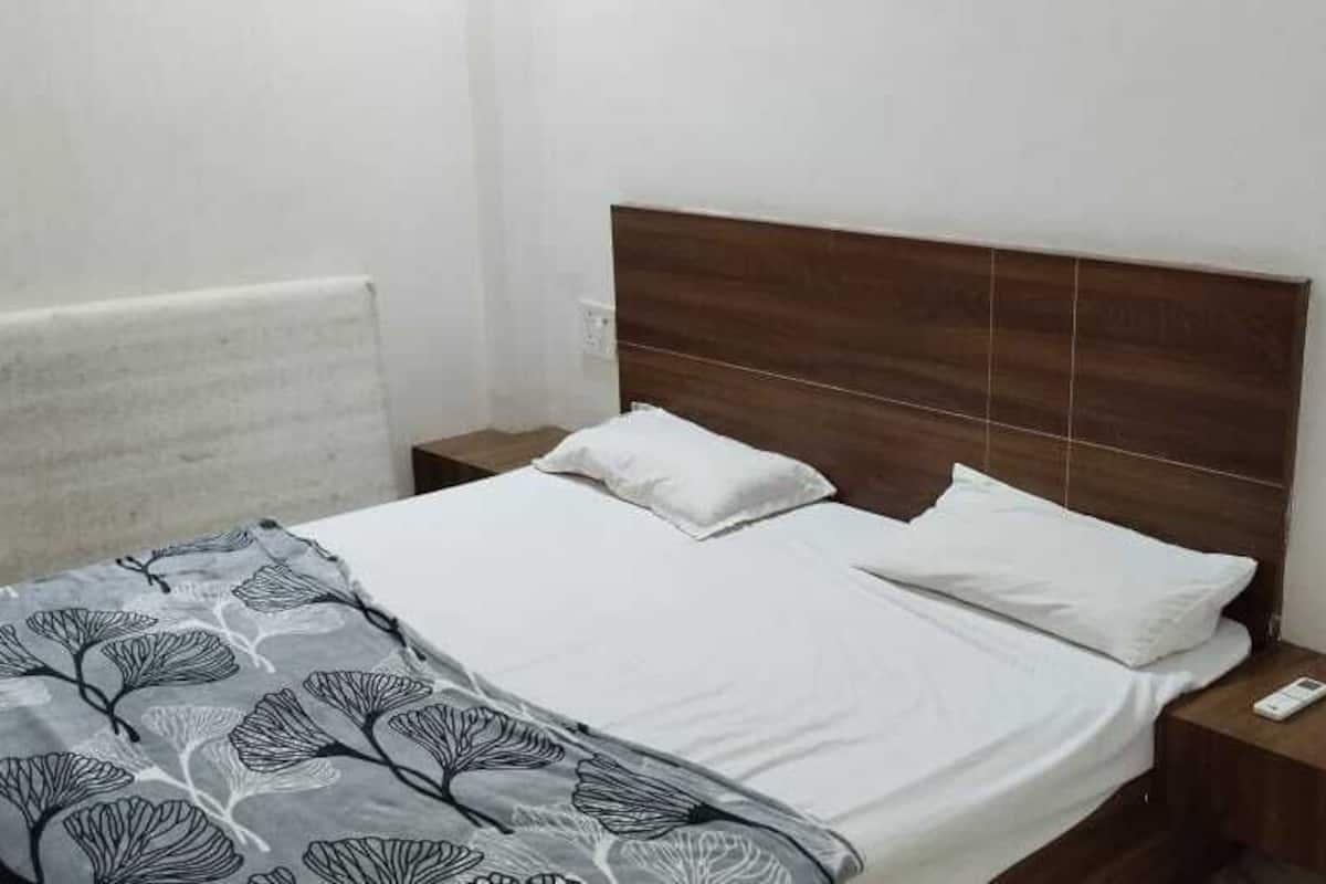 A single-bed room with a wooden headboard, white bedding, and a patterned throw blanket. There are two bedside tables, one with a phone and the other with a lamp.
