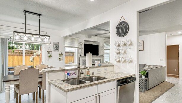A modern kitchen with a central island, built-in dishwasher, and a dining area with a table and chairs. - Fenced Yard & Fire Pit! Kennewick Family Retreat (Kennewick)