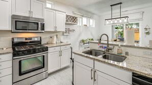 A modern kitchen with white cabinets, stainless steel appliances, a granite countertop, and a large window providing natural light. - Fenced Yard & Fire Pit! Kennewick Family Retreat (Kennewick)