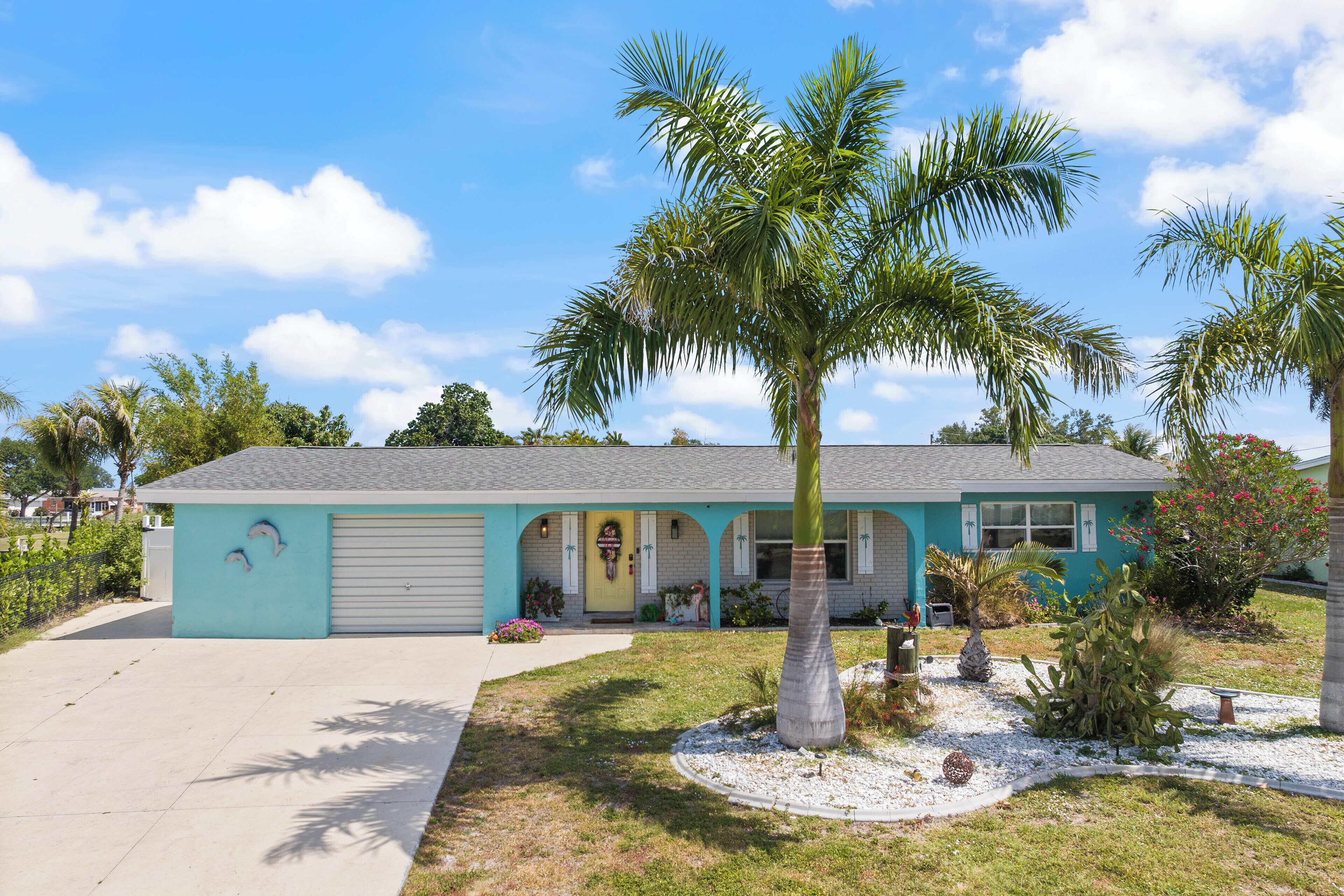 A two-story house with a garage, a front porch, and a well-maintained lawn with palm trees.