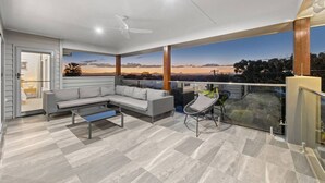 En moderne balkon med en grå hjørnesofa, et glasbord og en sort stol.