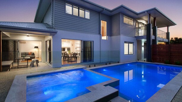 Et moderne hus med to etager, en swimmingpool, spiseplads og en terrasse med udendørs møbler.