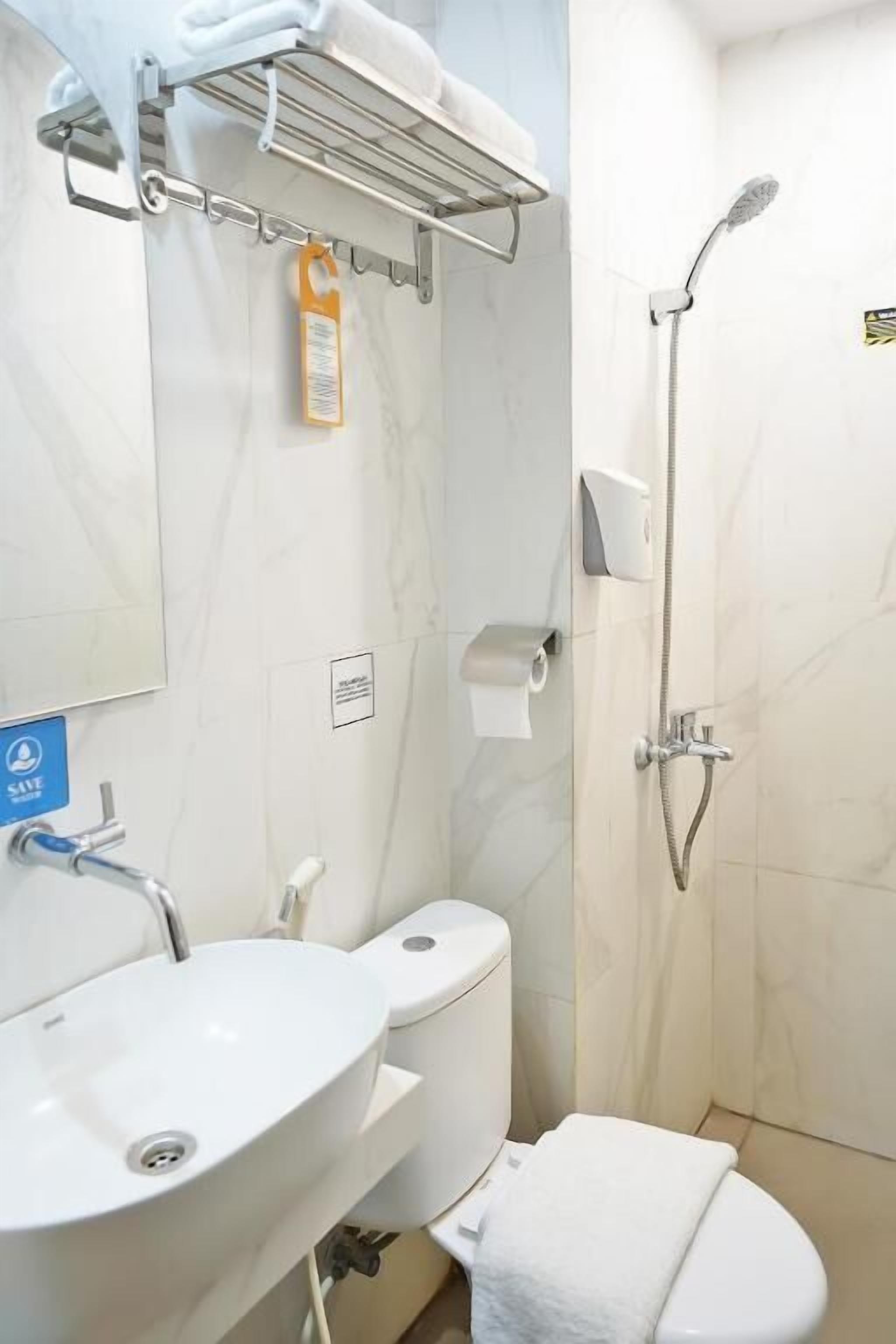 Un baño con lavamanos, inodoro y ducha de color blanco. Hay un perchero sobre el lavamanos y un dispensador de jabón en la pared.