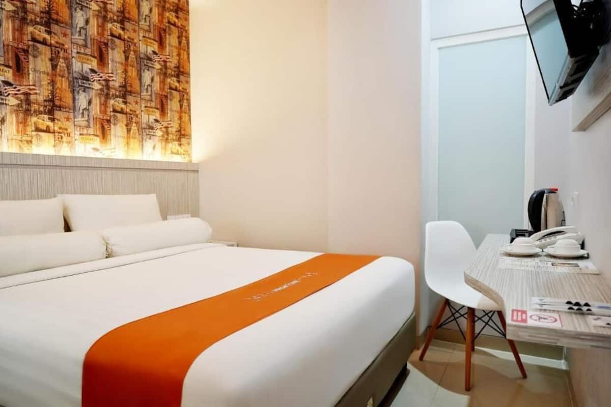 Una habitación de hotel con una cama, un escritorio, una silla y un televisor instalado en la pared.