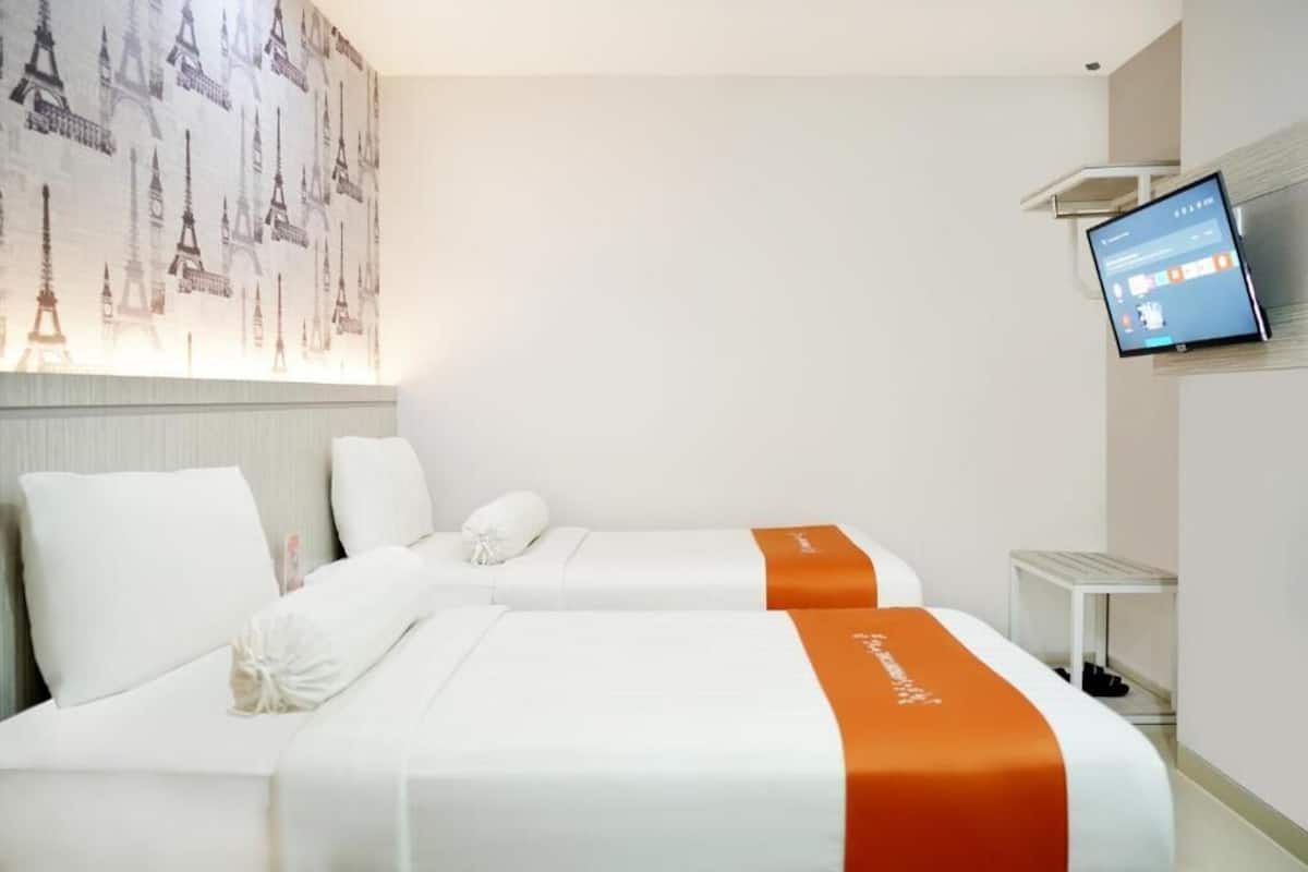 Habitación de hotel con dos camas, un televisor en la pared y una mesita.