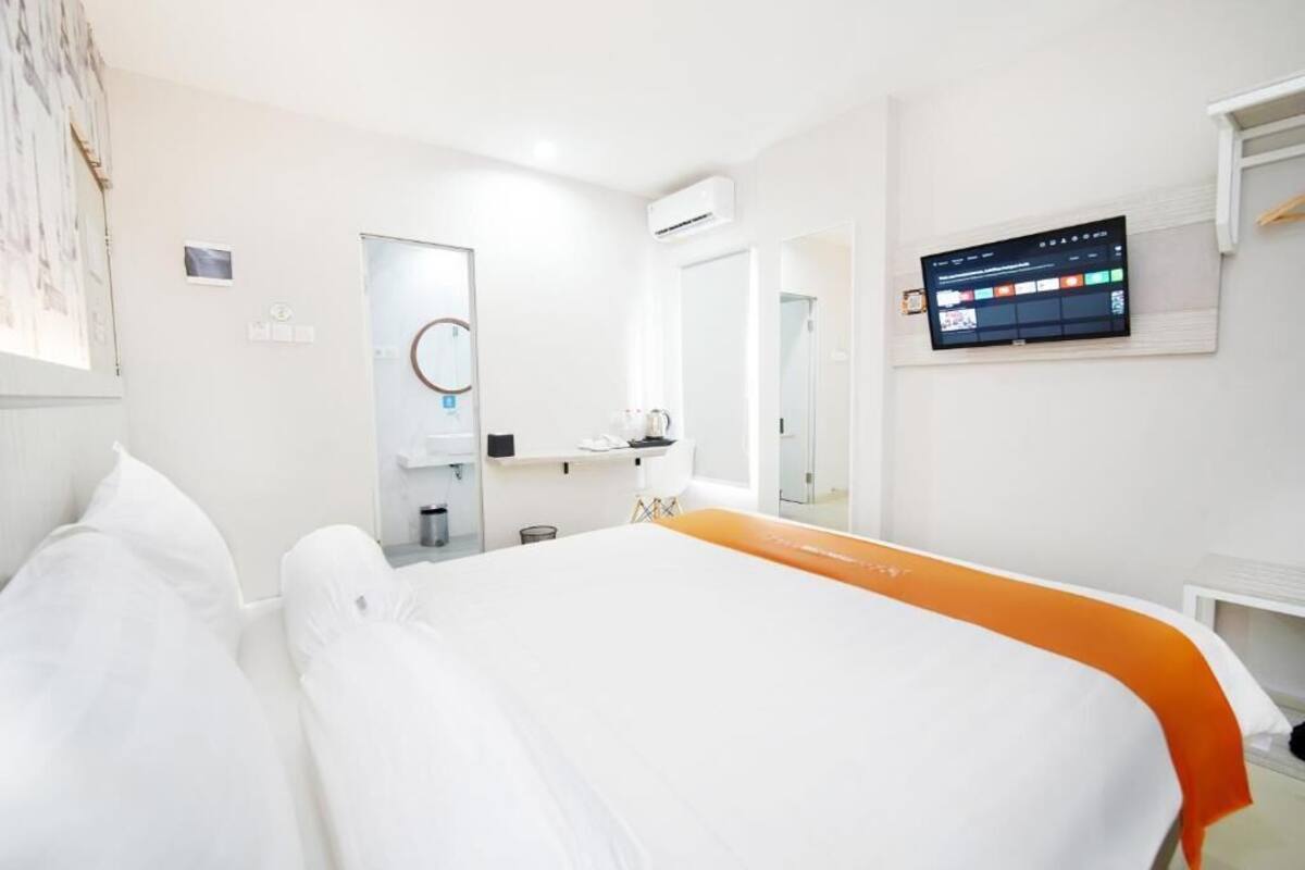 Habitación de hotel con cama, televisor montado en la pared, baño con espejo y unidad de aire acondicionado.