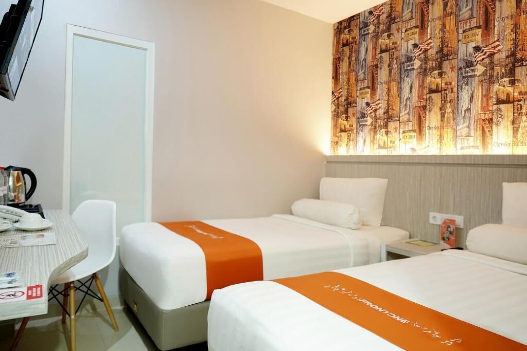 A hotel room with two single beds, a desk with a chair, and a wall with a patterned wallpaper.