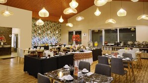 Uma área de refeições com várias mesas e cadeiras, um serviço de buffet e luminárias pendentes.