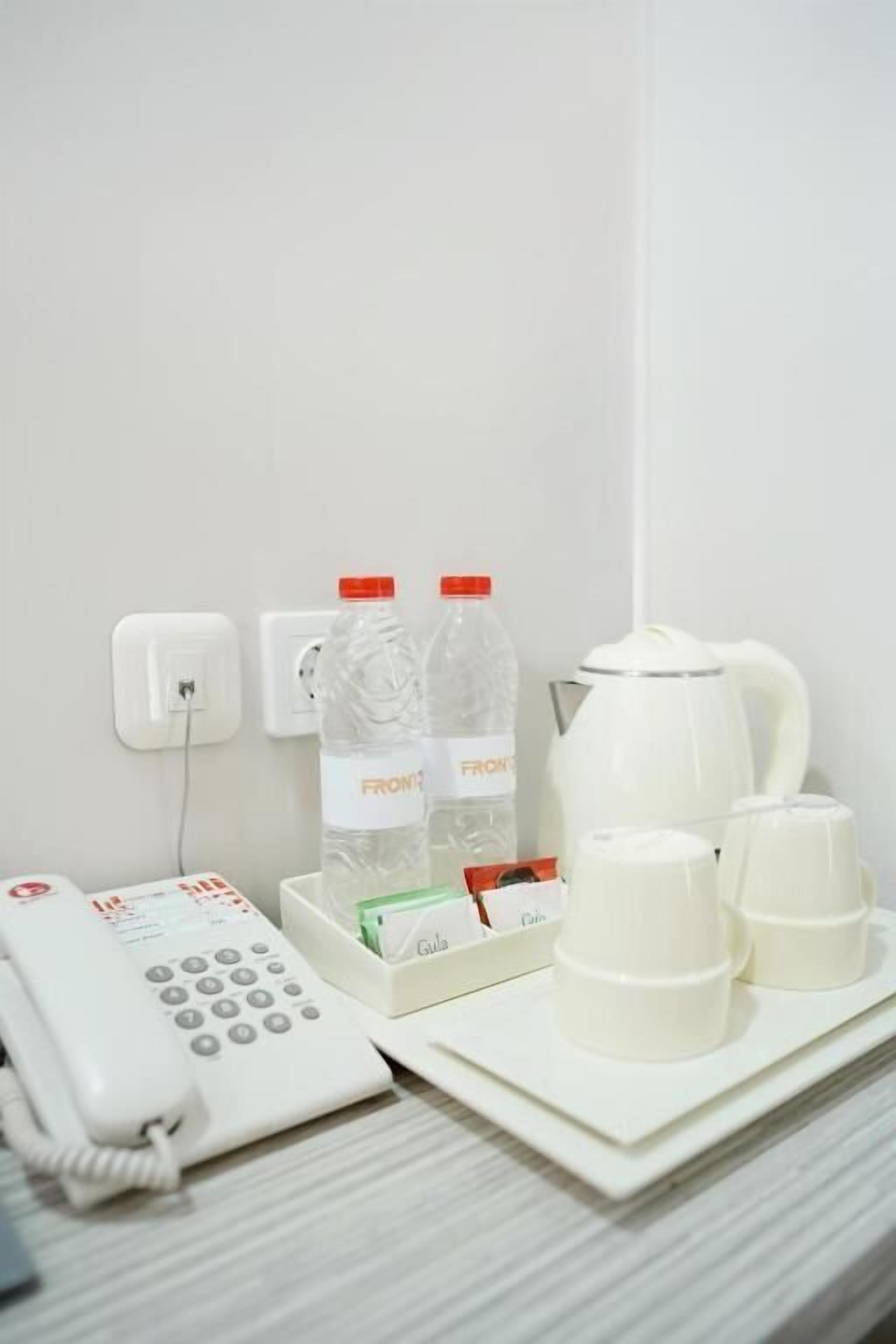 A hotel room with a white telephone, two water bottles, a coffee maker, and a tray with cups and a box of tissues.