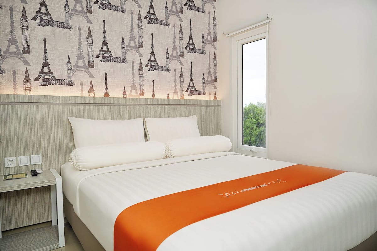 Habitación de hotel con cama, mesita de noche y ventana con vistas a zonas verdes.