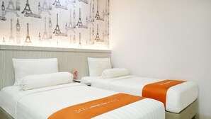 Duas camas com roupa de cama branca e colchas laranjas, uma mesa de cabeceira e uma parede com silhuetas da Torre Eiffel.