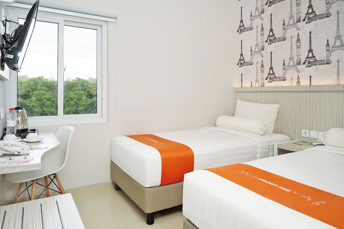 Habitación de hotel con dos camas, un escritorio con silla, ventana con vistas a zonas verdes y papel tapiz con motivos de París.