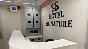Una reception di hotel con un bancone bianco e una targa a parete che riporta la scritta 'HOTEL SIGNATURE'.