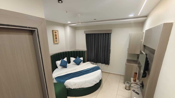 Una moderna camera d'albergo con un letto a ferro di cavallo, una televisione a schermo piatto e un mini-frigorifero.
