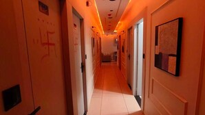 Un lungo e stretto corridoio d'albergo con porte su entrambi i lati, illuminato da luci calde.