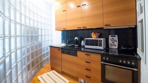 Een moderne keuken met houten kastjes, een zwart aanrecht, een magnetron, een fornuis en een raam met uitzicht op een gebouw.