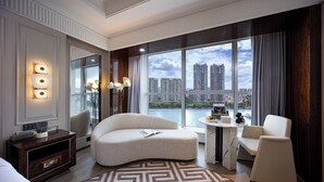 Ein modernes Hotelzimmer mit einer gebogenen Couch, einem kleinen runden Tisch und Blick auf hohe Gebäude und Wasser.