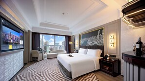 Ein Hotelzimmer mit einem großen Bett, einem Schreibtisch, einem Sessel, einer Sitzecke und einer Minibar, mit Blick auf die Stadt.
