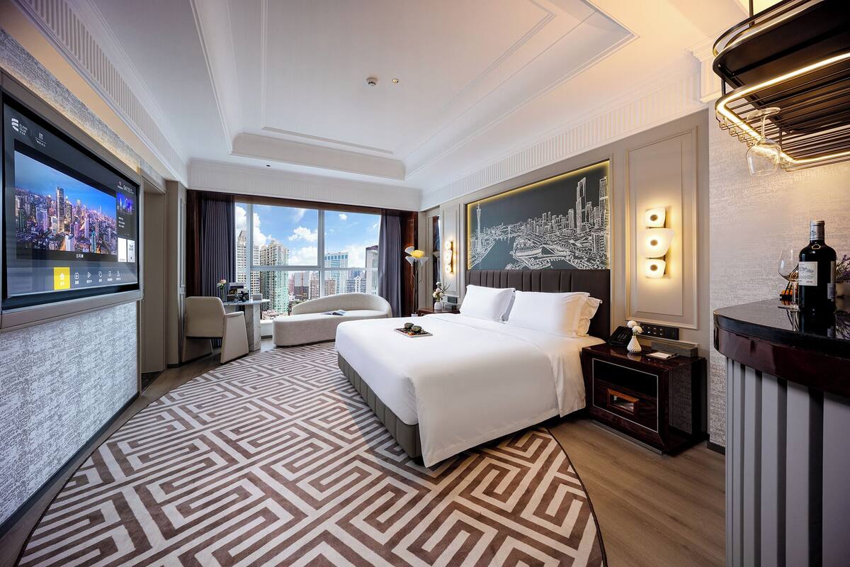 Habitación de hotel con una cama grande, un escritorio, una silla, un sofá, un minibar y vistas a la ciudad.