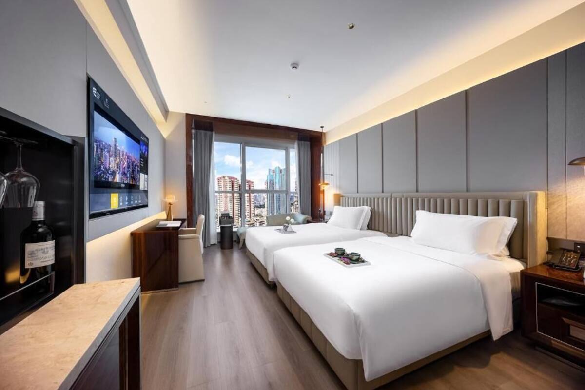 Habitación de hotel con dos camas, un televisor montado en la pared, vistas a la ciudad y un minibar.