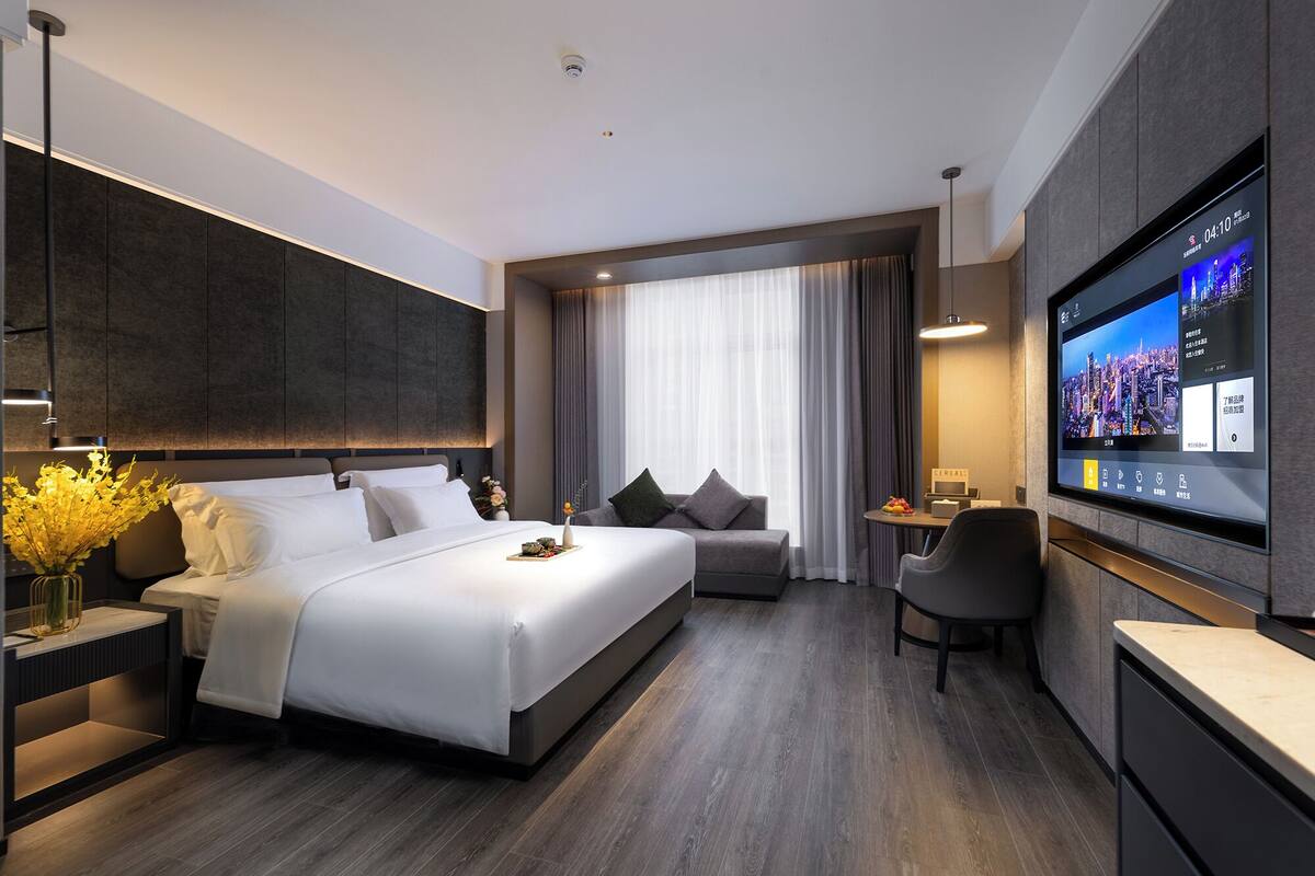 Una habitación de hotel moderna con una cama grande, un espacio de estar con un sofá y sillones, un televisor de pantalla plana y una pequeña mesa con una bandeja de comida.