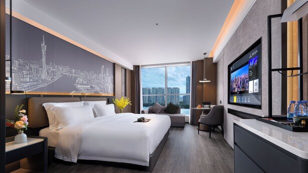 Ein modernes Hotelzimmer mit einem großen Bett, einem Schreibtisch, einem Fernseher und Blick auf die Stadt.